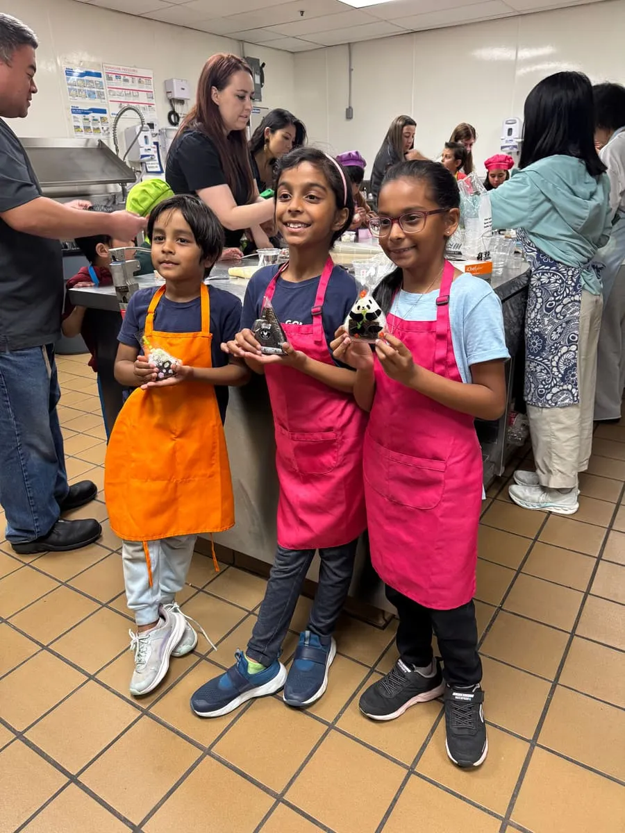 Three girls in aprons hold up decorated cupcakes.