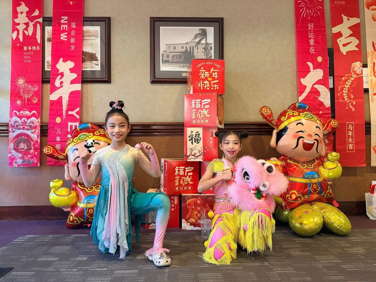 Two young dancers pose with Lunar New Year mascots in front of red couplets.