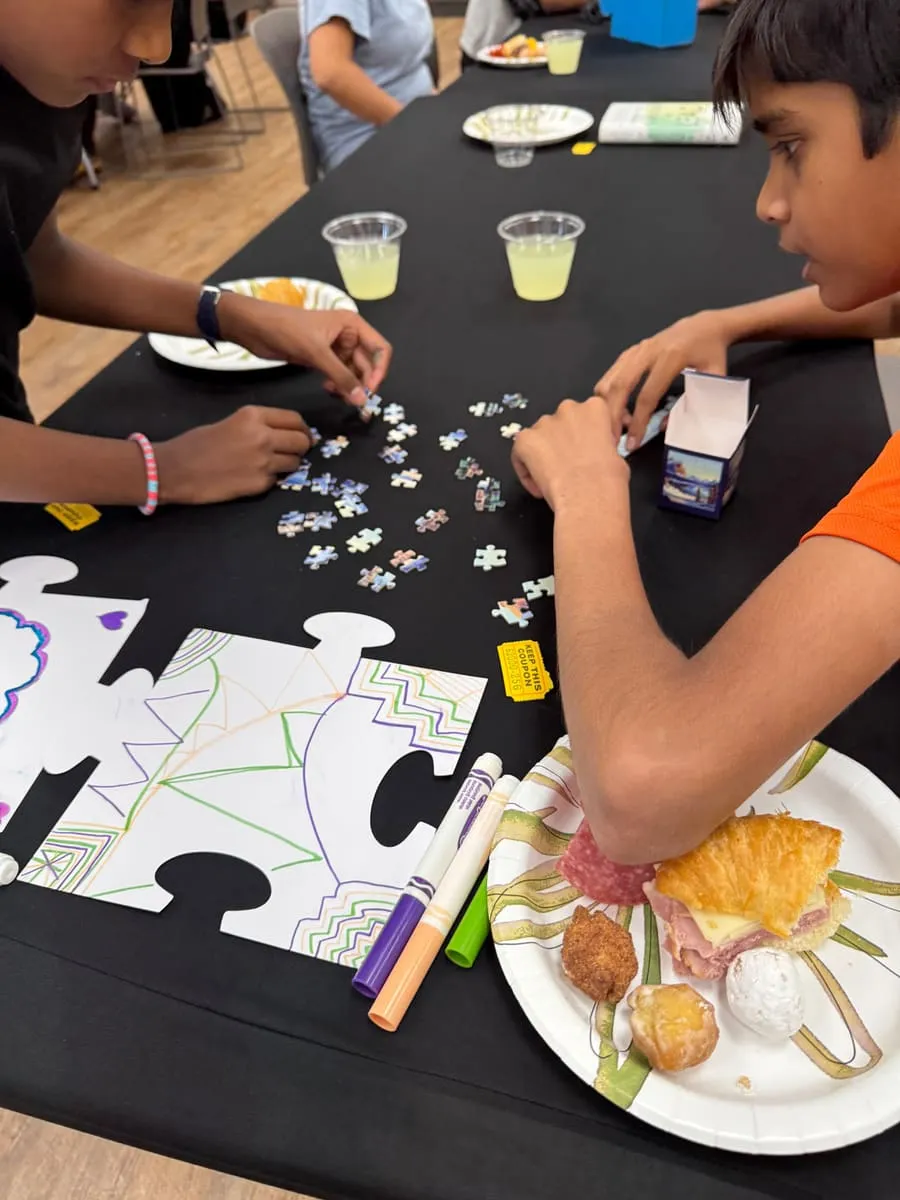Students piece together a jigsaw at a table covered in giant puzzle cut-outs.