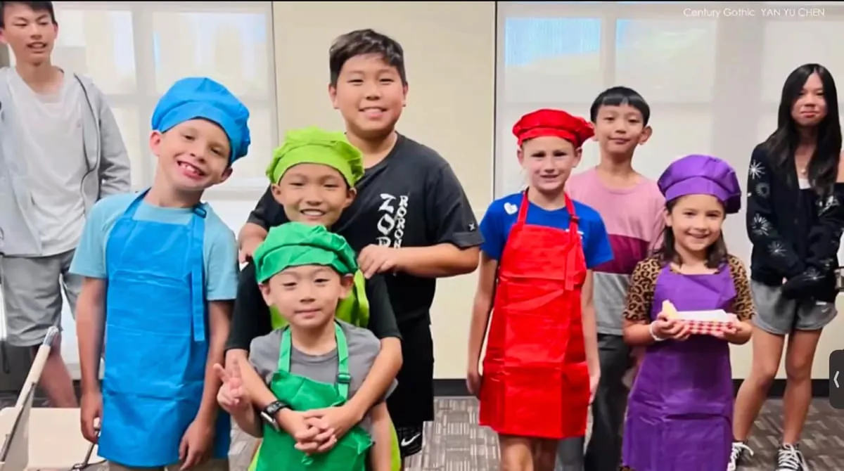 Children in colored chef hats and aprons line up in a kitchen.