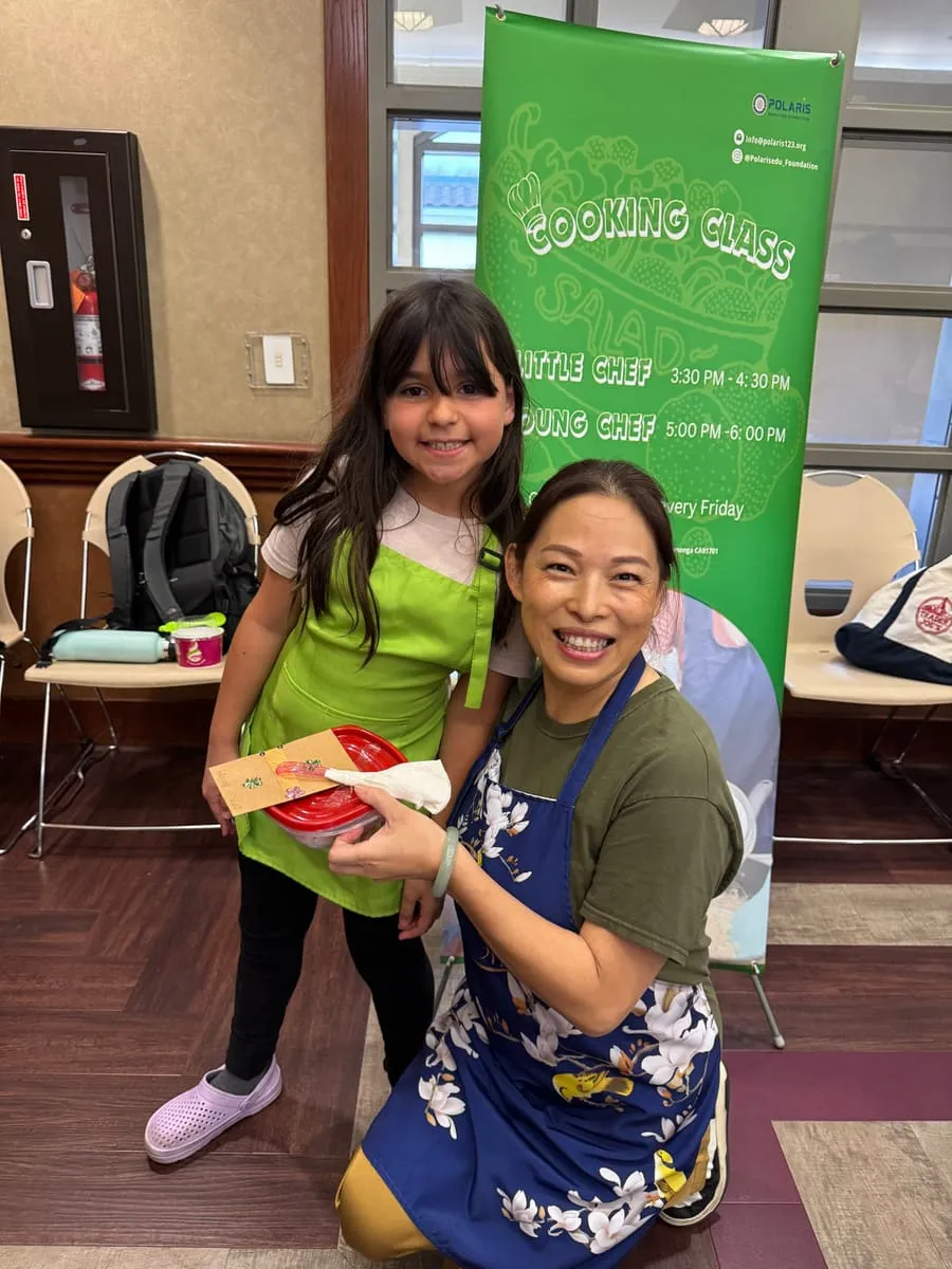 An instructor kneels beside a girl holding a box of food she made.