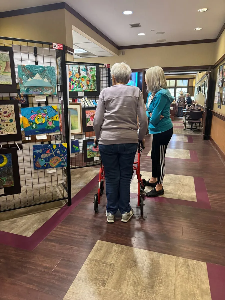 Two visitors walk between gridded panels hung with artwork.