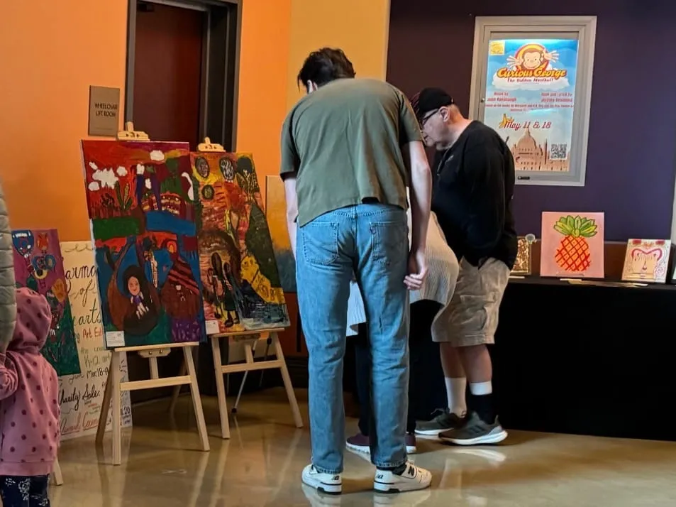 Visitors browse artwork set out on easels and a table.