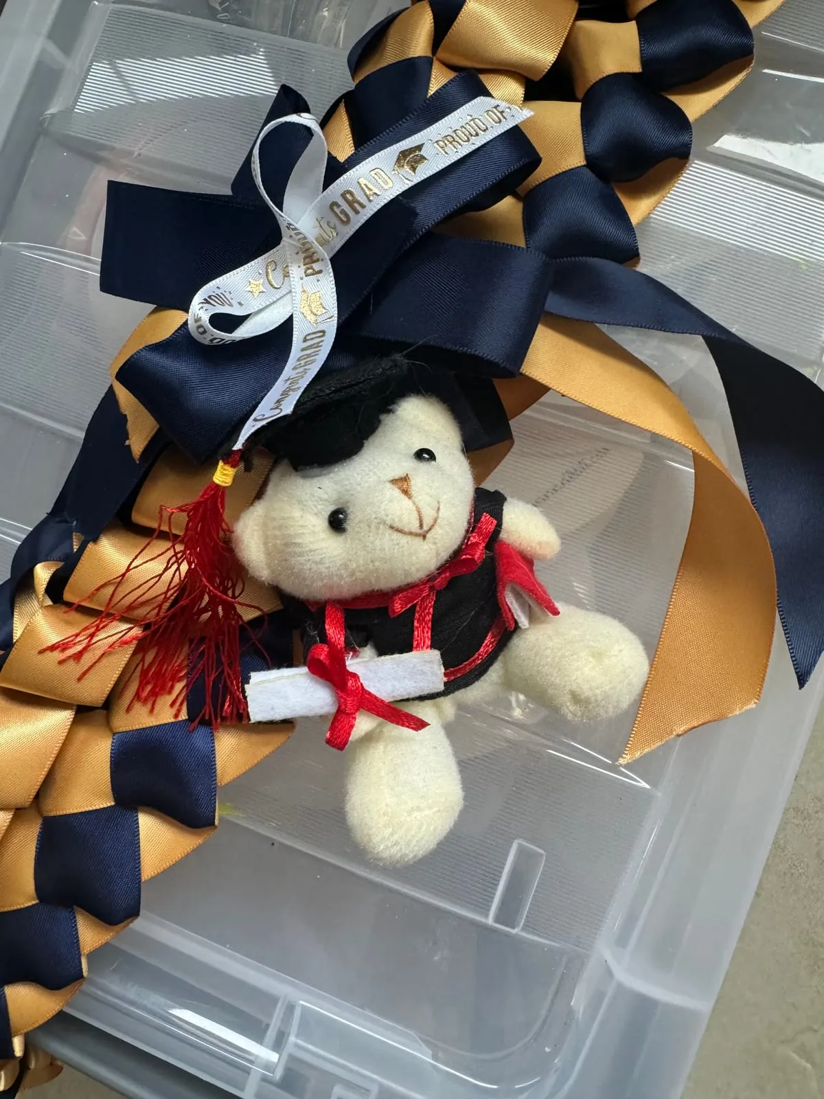 A navy and gold lei with a “Congrats Grad” ribbon and a small teddy bear in a graduation cap.